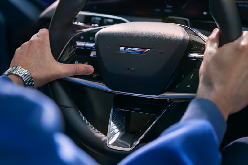 Close-up of a Man About to Press the V-Button on the 2026 OPTIQ-V Steering Wheel | Vaden Chevrolet of Hinesville in HINESVILLE GA